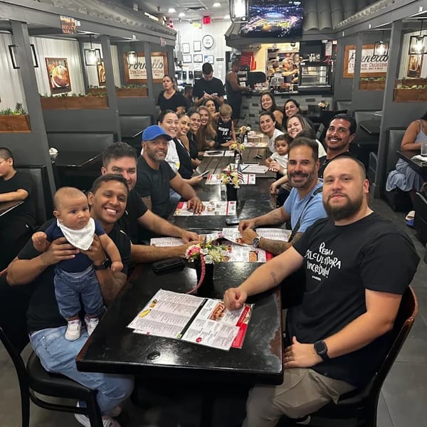 A large group of people, including children and babies, smiling and posing at tables in a restaurant.