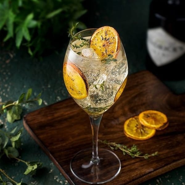 Sparkling cocktail with dried orange slices and herbs in a wine glass on a wooden board.