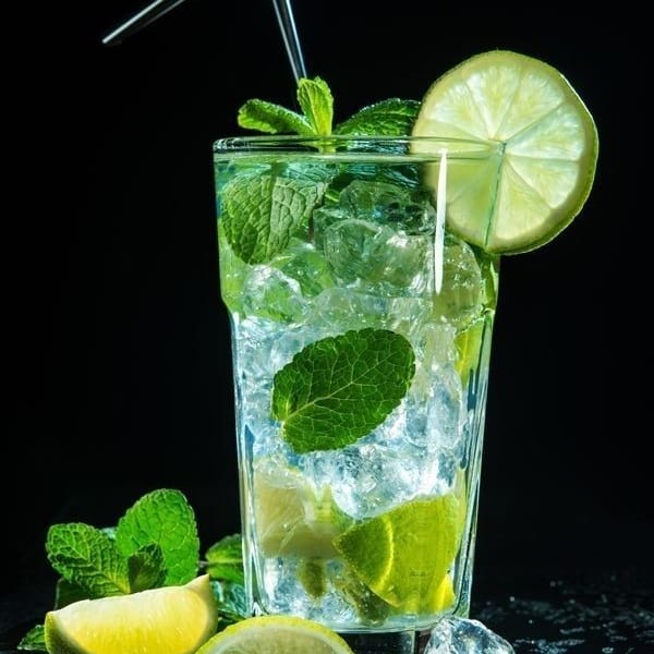 Refreshing mojito cocktail with ice, mint, lime slices, and a straw on a dark background.