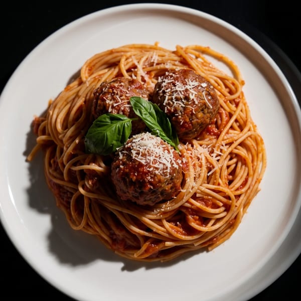Spaghetti and meatballs with tomato sauce, parmesan cheese, and basil on a white plate.