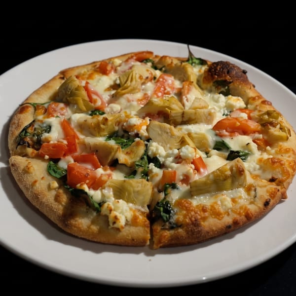 A white plate holds a pizza topped with artichoke hearts, tomatoes, spinach, and cheese.